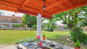 Un patio al aire libre con una pérgola de madera, una mesa lista para comer y plantas en macetas.