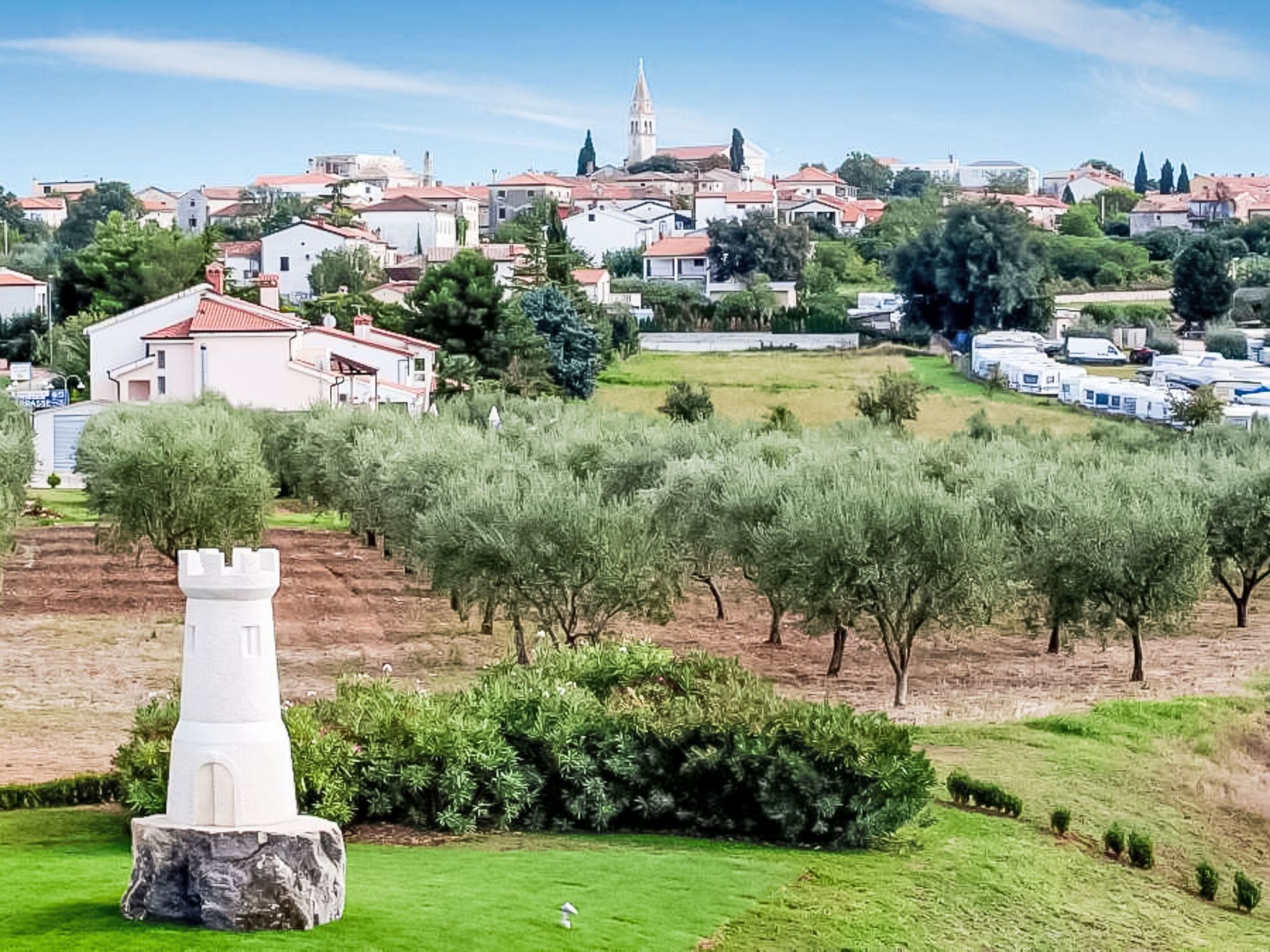 A town with a prominent church tower, residential buildings, and a white statue in a grassy area.