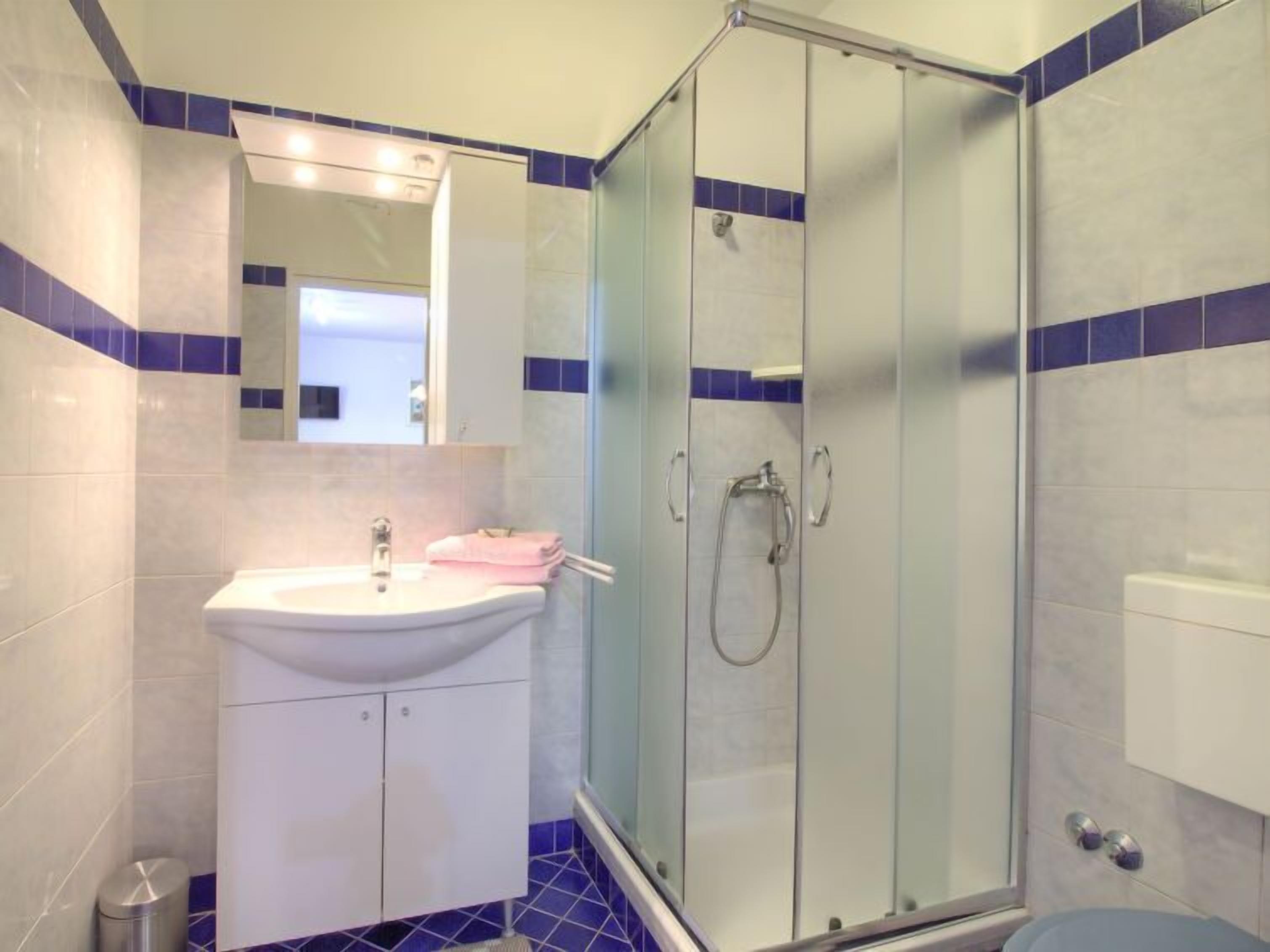A bathroom with a glass-enclosed shower, a sink with a mirror above it, and blue-tiled walls.