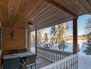 Eine hölzerne Veranda mit Tisch und Stühlen, mit Blick auf eine verschneite Landschaft mit Bäumen und einem Pavillon.