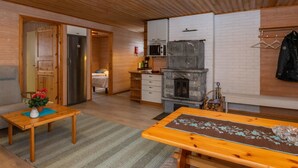 A cozy room with a wooden ceiling, a stone fireplace, a kitchen with a microwave, and a bed in the adjacent room.