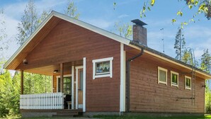 A wooden cabin with a porch, a chimney, and a small window.