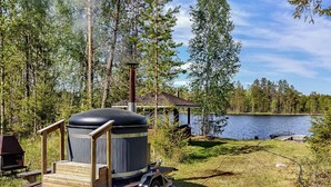 A portable grill with a chimney, a wooden deck, and a view of a lake surrounded by trees.
