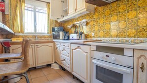 A kitchen with a microwave, toaster, and oven. There is a wicker chair and a sink. - Les Jardins de Sinople by Interhome (Saint Cyr sur Mer La Madrague)