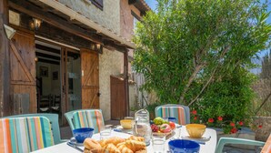 An outdoor dining area with a table set for two, featuring a basket of croissants, various bowls, and glasses. - Les Jardins de Sinople by Interhome (Saint Cyr sur Mer La Madrague)