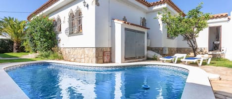 A house with a swimming pool, a stone wall, and a tiled roof.
