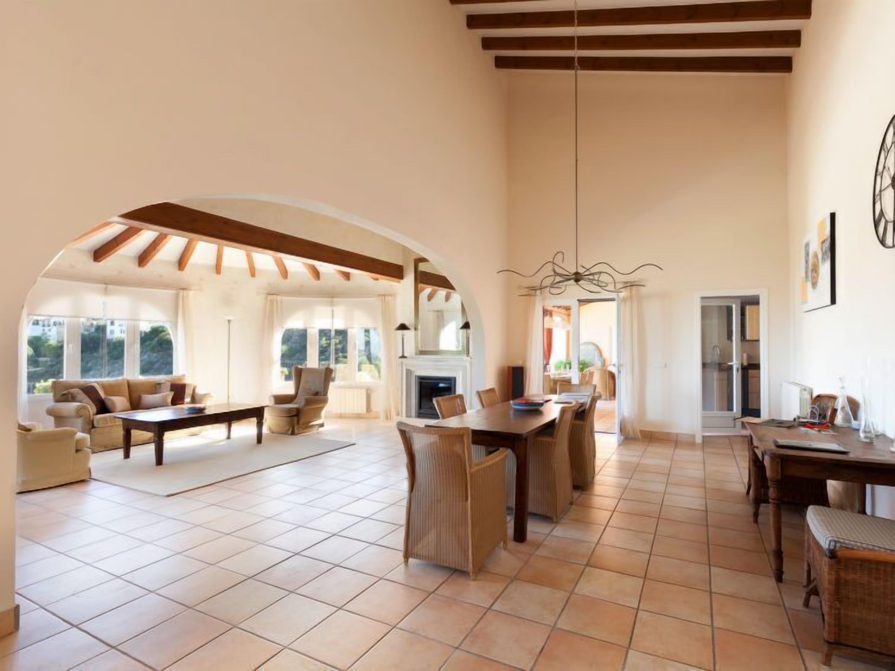A spacious living area with a high ceiling, large windows, and a fireplace.