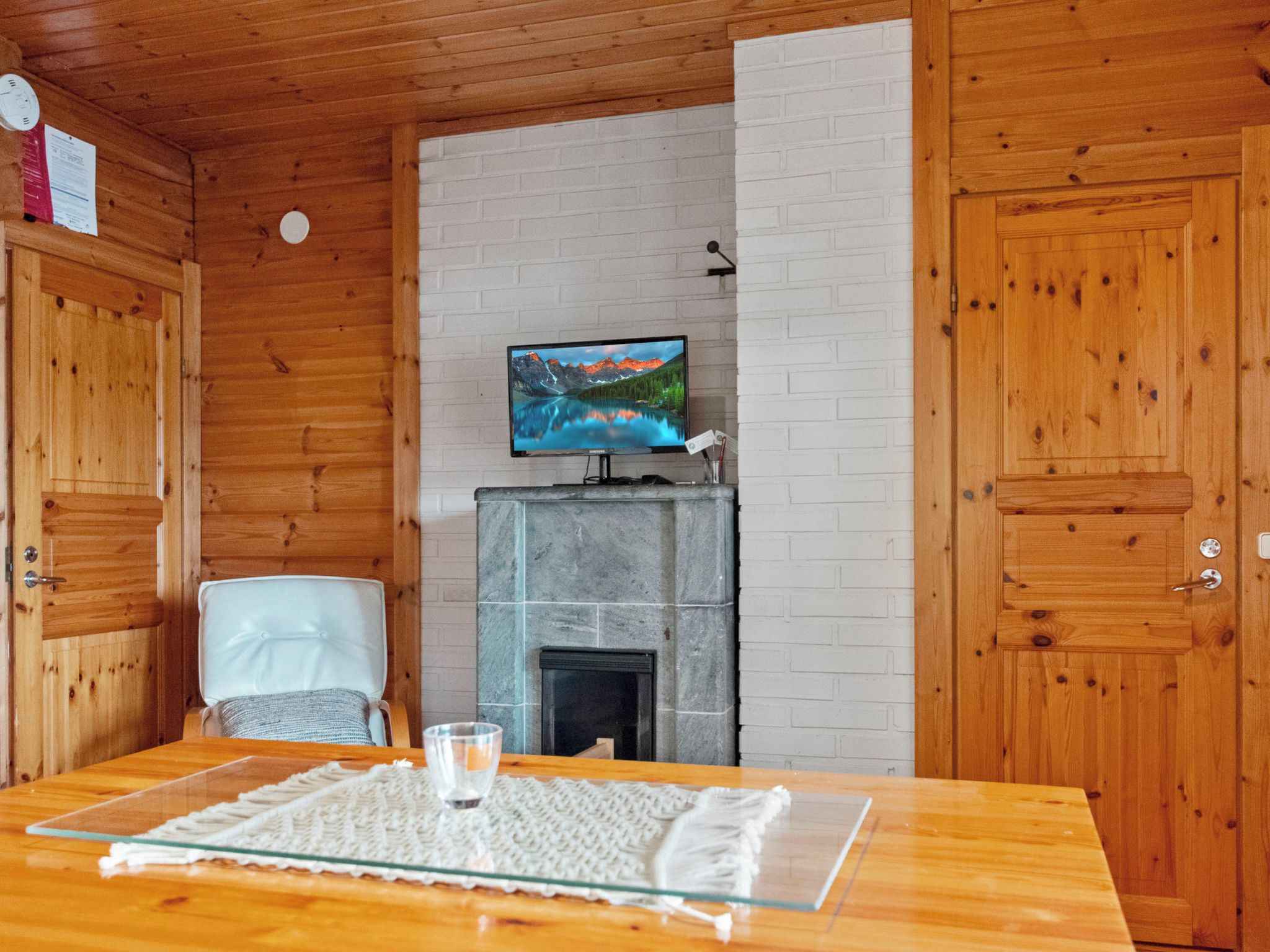 A wooden interior with a television on a mantel, a fireplace, and a dining table with a placemat.