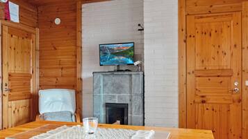 A wooden interior with a television on a mantel, a fireplace, and a dining table with a placemat.