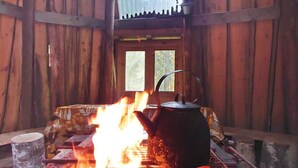 A rustic cabin interior with a wood-burning stove, a kettle, and a window with a view of trees. - Lahdenpohja, vaikon loma 7 by Interhome (Kaavi)