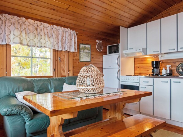 Un interior de cabaña acogedor con techo de madera, un sofá verde, una mesa de comedor de madera y una cocina con armarios y electrodomésticos blancos.