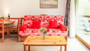 Een gezellige woonkamer met een rode en witte gestreepte bank, een houten salontafel en een schilderij aan de muur.