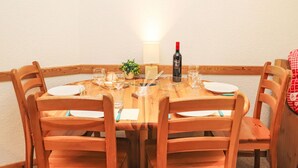Een houten eettafel met stoelen, een fles wijn, glazen en een kleine plant.