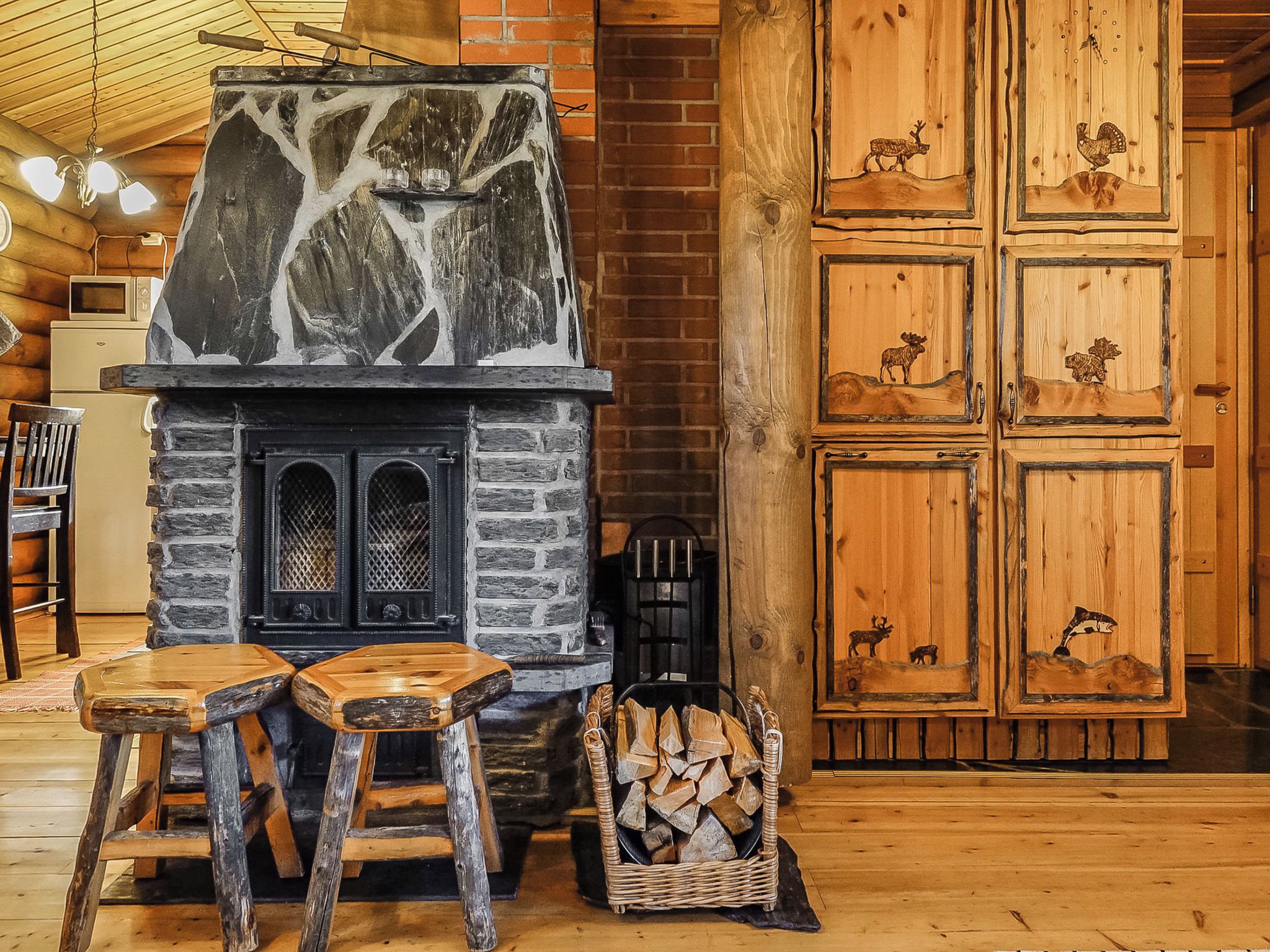 Un intérieur rustique avec une cheminée en pierre, des tabourets en bois et une pile de bois de chauffage.