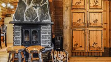Un intérieur rustique avec une cheminée en pierre, des tabourets en bois et une pile de bois de chauffage.