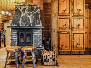 A rustic interior with a stone fireplace, wooden stools, and a stack of firewood.