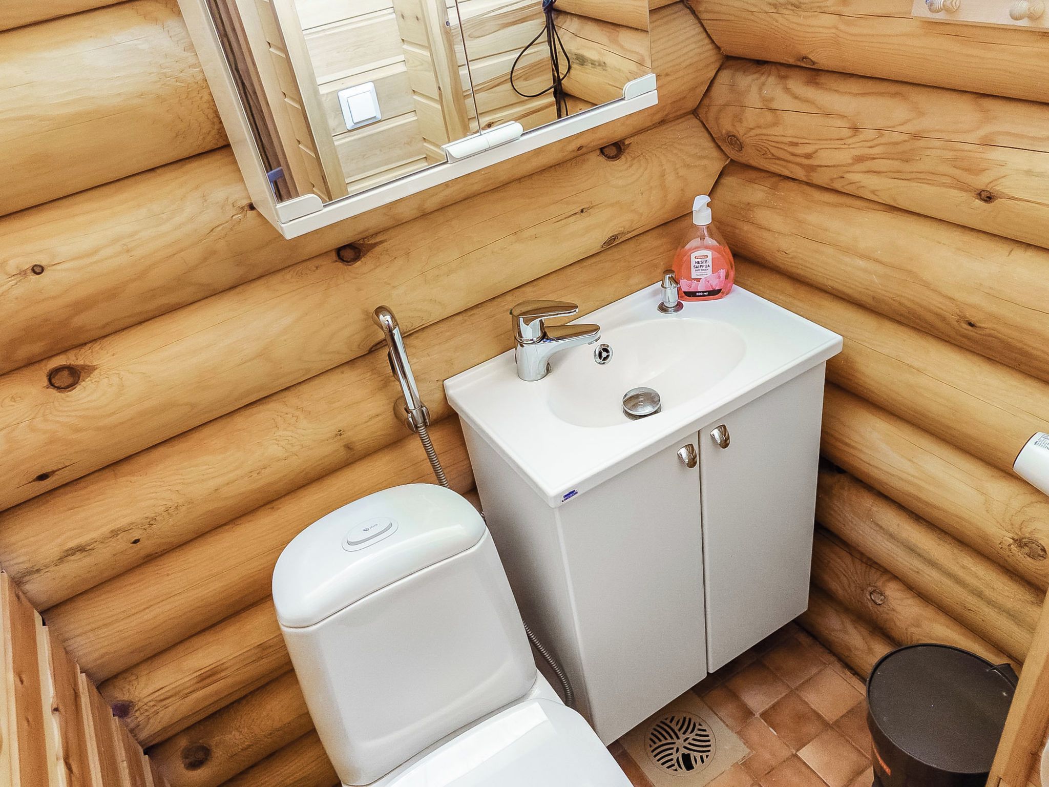 A compact wooden cabin bathroom with a white sink, a toilet, and a mirror above the sink.