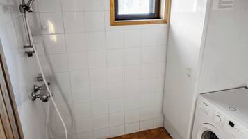 Une petite salle de bain propre, avec des carreaux blancs, une fenêtre en bois, une douche et un lave-linge.