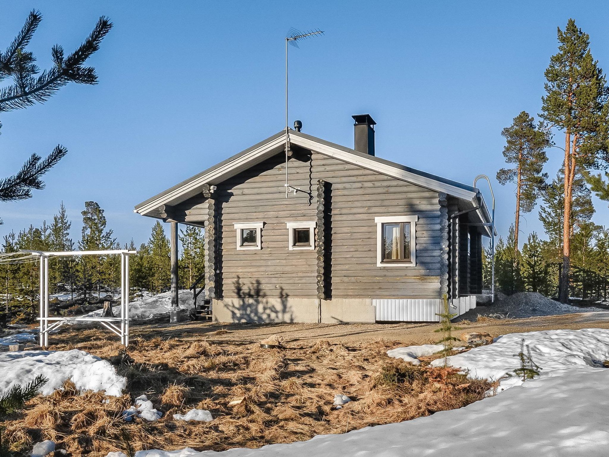 Hirsimökki, jossa on kalteva katto, savupiippu ja pieni kuisti.
