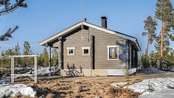 Hirsimökki, jossa on kalteva katto, savupiippu ja pieni kuisti.
