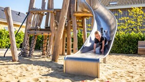 A playground with a slide and climbing structures on sandy ground.