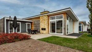 A modern two-story house with a stone facade, large windows, and a patio area with outdoor furniture.