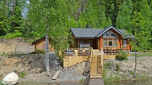 Eine Holzhütte mit einer Holzterrasse, die zu einem Steg über dem Wasser führt, umgeben von dichtem Wald.