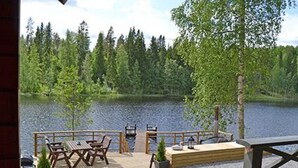 Eine Holzterrasse mit Gartenmöbeln mit Blick auf einen von Bäumen umgebenen See.