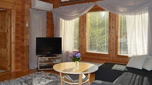 Ein gemütliches Blockhaushaus-Interieur mit Holzvertäfelung, einem Fernseher, einem runden Tisch mit Blumenvase und einer Couch.