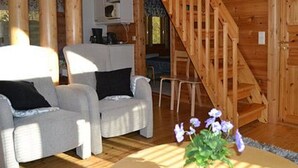 Ein Interieur einer Holzhütte mit einer Treppe, zwei Sesseln, einem Couchtisch und einer Blumenkomposition.