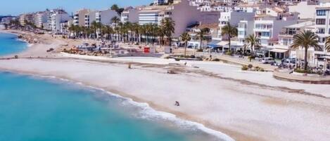A coastal town with a beach, white buildings, and palm trees.