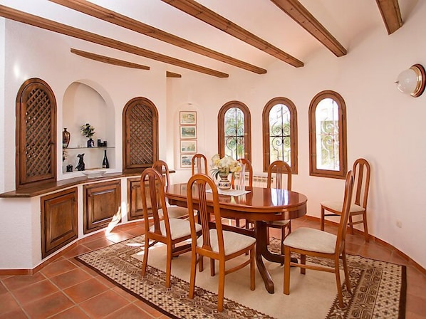 A dining area with a wooden table and chairs, arched windows, and a tiled floor.