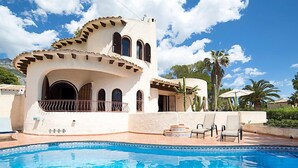 Una villa in stile mediterraneo con piscina, area relax esterna e palme.