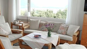 A cozy living room with a sofa, chairs, a coffee table, and a view of greenery through large windows. - Noisette by Interhome (Le Mont-Pèlerin)