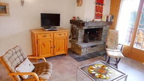 Una sala de estar con un sofá, una mesa de centro de vidrio, un televisor sobre un mueble de madera, una chimenea y un sillón.