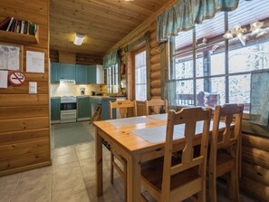 Un intérieur en bois comprenant une table à manger, des chaises, un coin cuisine et une fenêtre donnant sur un paysage agréable.