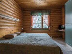Une pièce de cabane en bois comprenant un lit, un bureau et une fenêtre avec des rideaux.