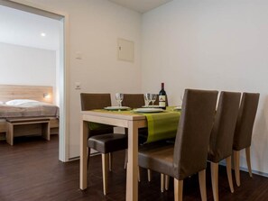 Un comedor con una mesa para dos, una botella de vino y una cama al fondo.