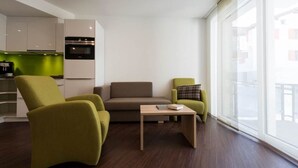 A modern living room with a sofa, two armchairs, a coffee table, and a kitchen area with white cabinets and a green backsplash. - Haus Alpenrose by Interhome (Saas-Almagell)