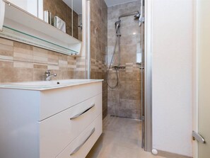 Un baño moderno con cabina de ducha de vidrio, tocador blanco con cajones y salpicadero de azulejos.