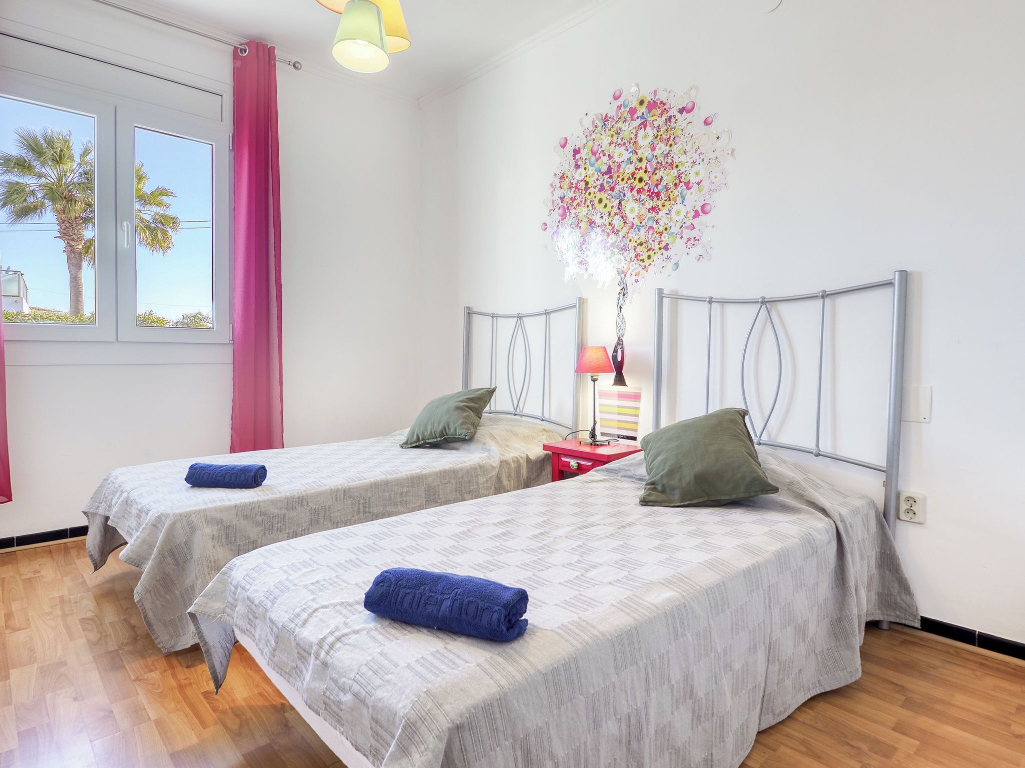 A bedroom with two beds, a window with curtains, a lamp, and a decorative wall piece.