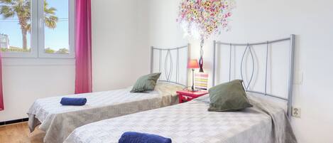 A bedroom with two beds, a window with curtains, a lamp, and a decorative wall piece.