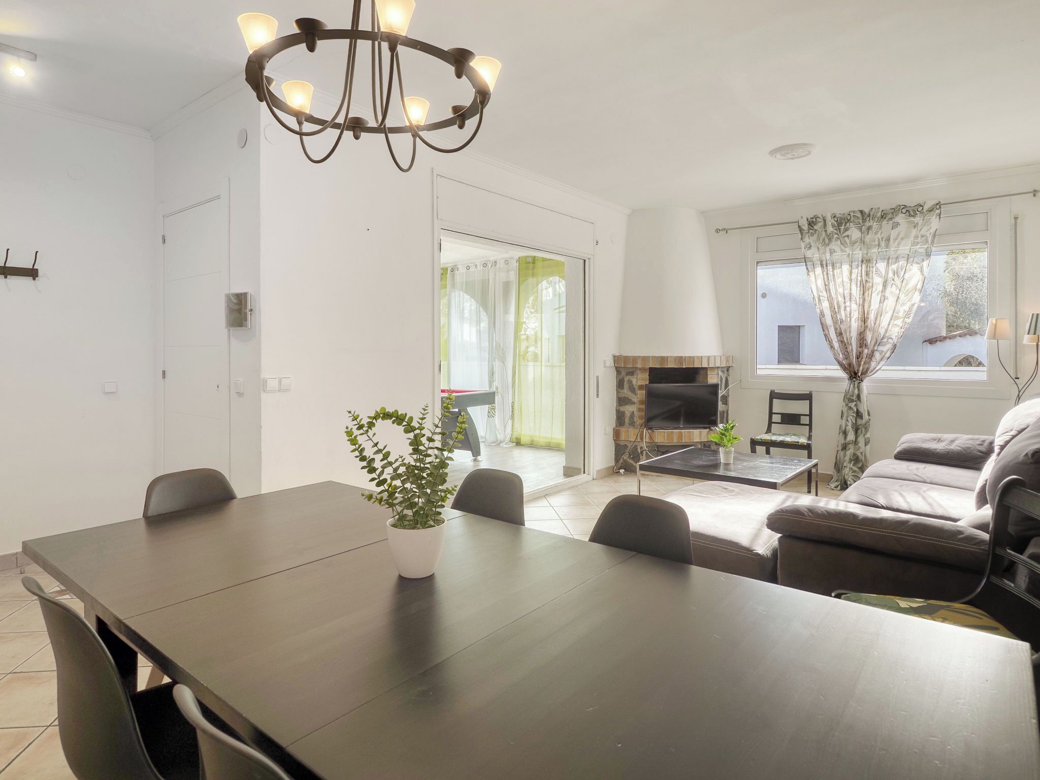 Una sala de estar moderna con una mesa de comedor de madera oscura, una araña, un sofá y una chimenea.