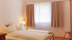 A hotel room with a bed, a nightstand, a lamp, and a window with curtains. - Chesa Sur Val 22 by Interhome (St. Moritz)