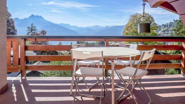 A balcony with a table and chairs, overlooking a mountainous landscape. - Ermitage 11 by Interhome (Villars)