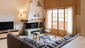 A modern living room with a large sectional sofa, a flat-screen TV, a fireplace, and a large window with curtains. - Ermitage 11 by Interhome (Villars)