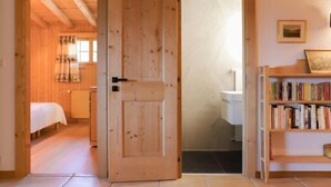 A wooden interior with a bed, a bookshelf, and a bathroom visible through an open door. - Ermitage 11 by Interhome (Villars)