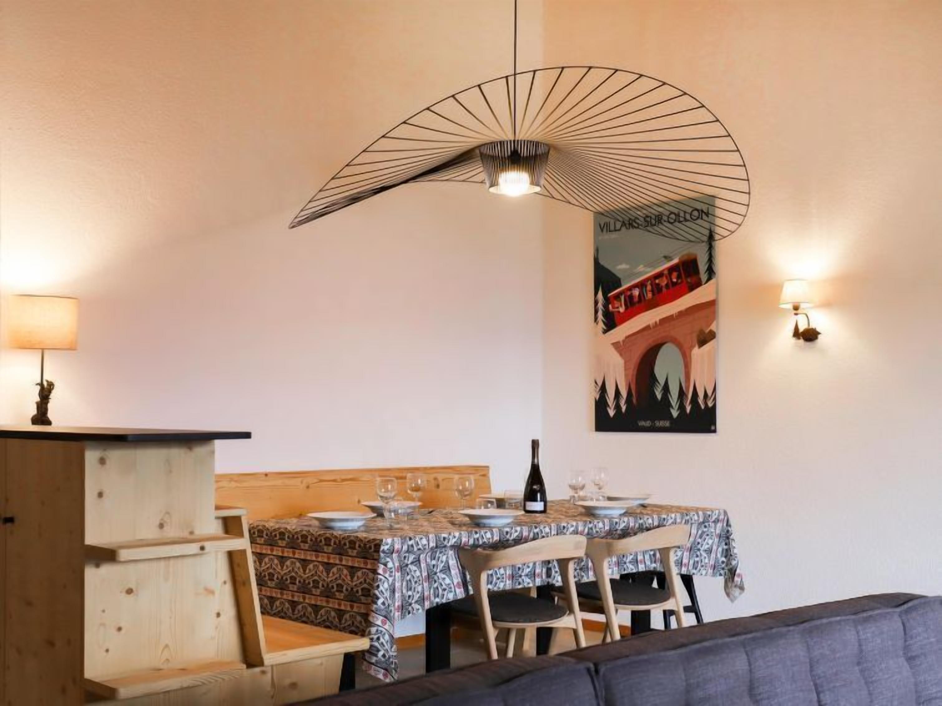 A dining area with a table set for four, a wine bottle, and a poster on the wall.