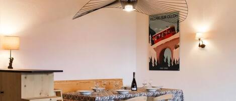 A dining area with a table set for four, a wine bottle, and a poster on the wall.