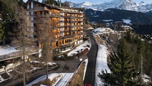 Un hotel a più piani con balconi, una località sciistica sullo sfondo e un paesaggio innevato.